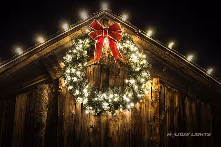 Barn Christmas lights installation with warm white roofline lighting and festive wreath decoration in Massachusetts Barn Christmas lights installation with warm white roofline lighting and festive wreath decoration in Massachusetts